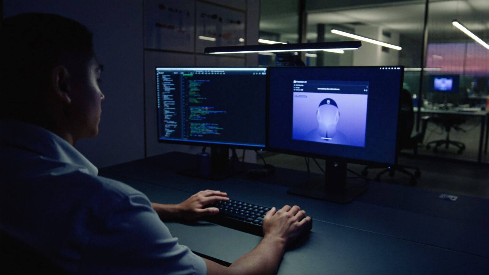Developer working at a two-monitor workstation in a dark office