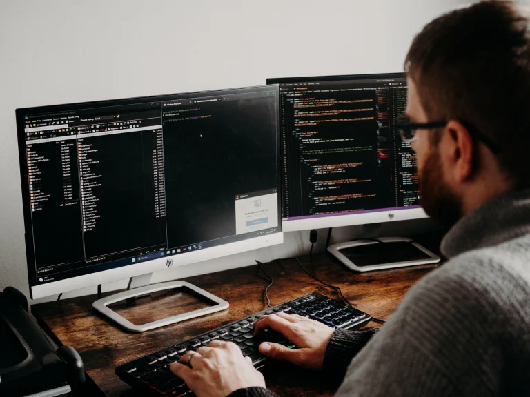 Software developer working at a desk with two monitors displaying code